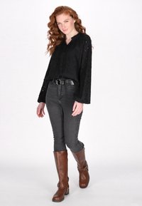 Blusa nera in tessuto con texture e maniche lunghe, abbinata a jeans scuri aderenti grigi e stivali in pelle marrone al ginocchio con fibbie.