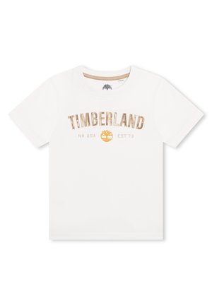 T-shirt en coton blanc mettant en avant le mot "TIMBERLAND" imprimé en doré, avec "NH. USA EST73" et un logo jaune en dessous. Manches courtes, col rond.
