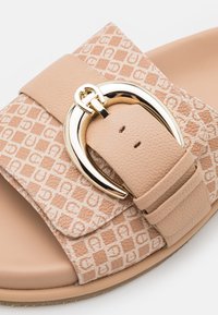 Sandale à glissière beige avec un dessus en cuir texturé présentant un motif de carrés et de lettres. Boucle dorée comme accent notable.