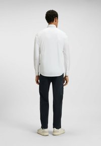 Vit långärmad skjorta med knappmanschetter, kombinerad med mörka byxor med sidofickor, kompletterad med beige sneakers.