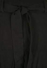 Schwarzes Stoffkleid mit einem gebundenen Gürtel. Das Material wirkt glatt mit einem matten Finish, was das taillierte Design betont.