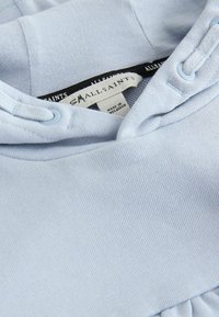 Hanorac bleu deschis cu țesătură texturată, prevăzut cu glugă cu șnur, tiv cu revere și cusături decorative. Eticheta brandului este vizibilă.