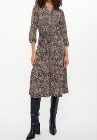 Černo-béžové šaty s vzorem, výstřihem do V, tříčtvrtečními rukávy a stahovaným pasem. Kombinované s černými kozačkami nad kolena na podpatku.