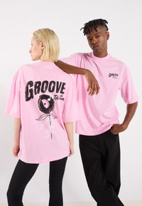 Pink oversized t-shirts with black graphic print; front features "Groove" logo, back has a hand holding a rose design.