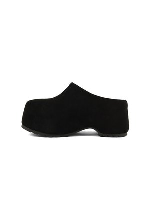 Sabot à plateforme en suède noir avec un talon compensé haut et un bout arrondi, vu de côté sur fond blanc.