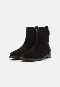 Stivaletti neri in suede con una superficie liscia, suola piatta in gomma, cerniera laterale e inserti elastici per facilitare l'indossamento.