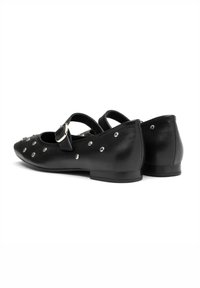 Bailarinas de cuero negro con punta afilada, tira delgada con hebilla y tachuelas plateadas a lo largo de los lados. Tacón plano y textura suave.