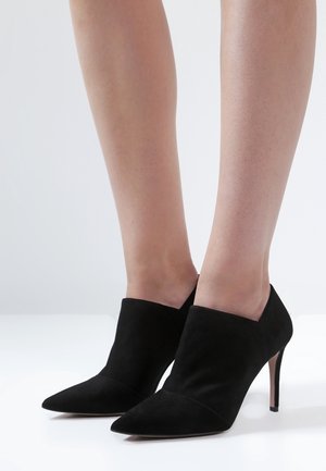 Bottines en daim noir avec un bout pointu et un design élégant. Elles présentent un talon fin et une tige découpée pour un look contemporain.