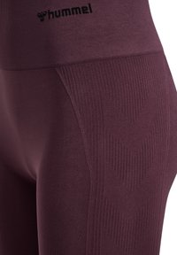 Leggings de sport bordeaux avec une texture côtelée, présentant un motif en chevron sur le côté et un logo noir au niveau de la taille.