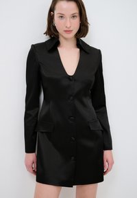 Schwarzes Satin-Kleid mit langen Ärmeln, tiefem V-Ausschnitt, sechs vorderen Knöpfen und zwei aufgesetzten Taschen. Glatte Textur und maßgeschneiderte Passform.