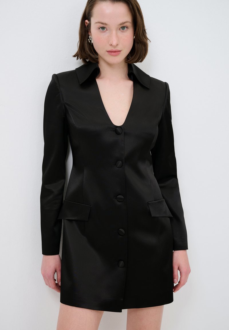 Schwarzes Satin-Kleid mit langen Ärmeln, tiefem V-Ausschnitt, sechs vorderen Knöpfen und zwei aufgesetzten Taschen. Glatte Textur und maßgeschneiderte Passform.
