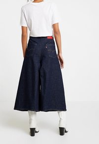 Tummansiniset farkkukangasta leveälahkeiset culottes, joissa on takataskut. Yhdistetty valkoiseen t-paitaan ja valkoisiin korkokenkiin, korostaen tekstuurien kontrastia.