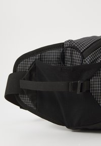 Black bag with a grid pattern. Features textured fabric, a strap, and multiple compartments. The interior shows a checkered design.