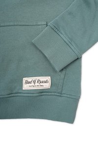 Valkoinen teal-huppari, jossa on ribbireunat ja pieni "Band of Rascals" -merkki ommeltuna kankaaseen brändäystä varten.