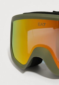Χειμερινά γυαλιά σκι σε ελαιόπρασινο χρώμα με ανακλαστικούς πορτοκαλοκίτρινους φακούς και μαύρη αφρώδη επένδυση, με το λογότυπο "EA7" στο πάνω δεξί μέρος.