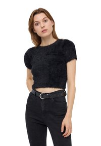 Maglione corto nero con maniche corte, texture pelosa e scollatura rotonda, abbinato a jeans neri con decorazioni e una cintura.