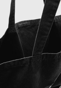 Zwarte canvas boodschappentas met versterkte handvatten, met een gestructureerd oppervlak en een logolabel aan de binnenkant. Eenvoudig, ruim ontwerp voor veelzijdig gebruik.