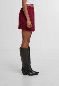 Vínová plisovaná sukně s žebrovaným pasem, spárovaná s vysokými černými koženými botami na podpatku se špičatou špičkou.