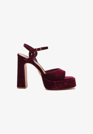 Sandali platform in velluto bordeaux con tacco quadrato alto, punta aperta e cinturino alla caviglia fissato con una fibbia. Texture liscia.