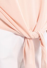 Tessuto leggero color pesco annodato in vita, abbinato a un indumento bianco. Visibili la trama morbida e la finitura liscia.