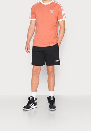 Pomarańczowa koszulka z krótkim rękawem z białym wykończeniem, czarne szorty sportowe i czarne sneakersy za kostkę z białymi paskami oraz logo.