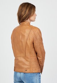 Bruine leren jas met een getailleerd ontwerp, voorzien van textuurpanelen, een staande kraag en metalen accenten aan de onderzoom.