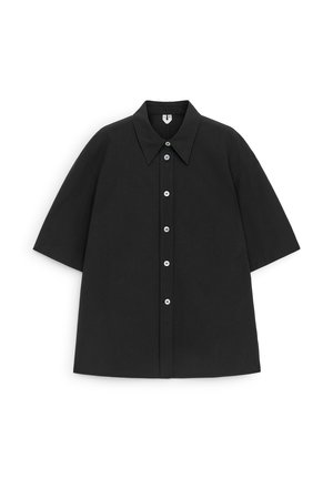 Chemise noire à manches courtes avec un col pointu et cinq boutons blancs sur le devant, présentée à plat sur un fond blanc.