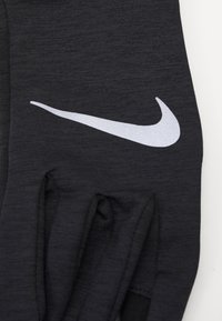 Guanto sportivo nero con texture a coste, con un prominente logo Nike bianco nella zona del polso. Progettato per prestazioni e comfort.