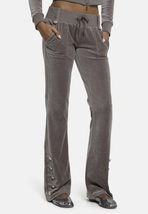 Γυναίκα που φοράει γκρι βελουτέ παντελόνι με εμπρόσθιες τσέπες, κορδόνι στη μέση, με λεπτομέρειες κουμπιών στις μανσέτες, συνδυασμένο με ασημένιες μπαλαρίνες.