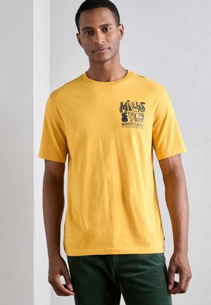 Gul bomulds T-shirt med rund hals og korte ærmer, der har et grafisk tryk på den øverste venstre side i sort.