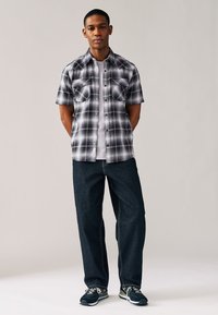 Kortärmad rutig skjorta i svart och vitt med två bröstfickor, kombinerad med mörka jeans och svarta sneakers.