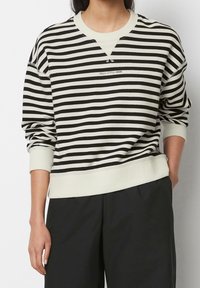 Felpa a righe in nero e crema. Tessuto morbido, design a manica a V, polsini e orlo a coste, e un piccolo logo sul petto.