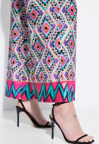 Färgglada mönstrade culotter med diamant- och zigzag-mönster i rosa, lila och turkos, tillsammans med svarta remsandaler med hög klack.