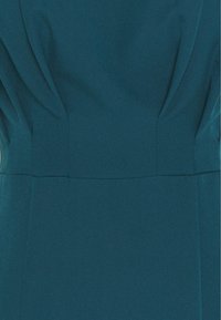 Robe bleu sarcelle avec une texture lisse, présentant des détails plissés aux épaules et une taille cintrée, créant une silhouette structurée.