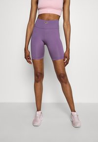 Violetit, korkeavyötäröiset pyöräilyshortsit joustavasta kankaasta. Ominaisuutenaan kultainen logokoriste. Yhdistetty istuvaan vaaleanpunaiseen urheiluliiviin ja vaaleanpunaisiin tennareihin.