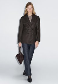 Dunkler, doppelt knöpfbarer Blazer, gestreiftes Oberteil, lockere, dunkle Jeanshose, schwarze Schuhe und kleine braune Handtasche; glatte Textur und maßgeschneiderter Schnitt.