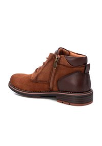 Botas de ante marrón a la altura del tobillo con un tacón de cuero marrón liso, que cuentan con cordones y un zipper lateral. Diseñadas con una suela de goma resistente y acentos de costura.