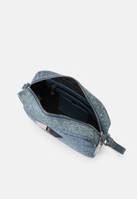 Denim torba preko tijela s zatvaračem, unutarnjim džepovima i glatkim plavim remenom. Ima metalni detalj sprijeda.