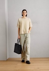 Beige oversized genser, lysegrøn vide bukser, svart tote bag og svarte sko. Enkle, jevne teksturer med et avslappet design.