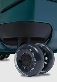 Donkergroene koffer met zwarte accenten en twee doorzichtige wielen, met een gestructureerd oppervlak en een zichtbaar merklogo op het wiel.