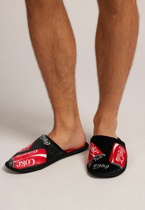 Zapatillas de casa de color negro y rojo, con el logo de Coca-Cola y diseños de latas de bebida, hechas de una tela suave y con suelas planas.