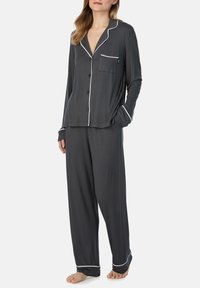 Set di pigiama in satin grigio con camicia a maniche lunghe, dettagli in piping bianco, chiusura a bottoni e tasca. Pantaloni morbidi con dettagli coordinati.