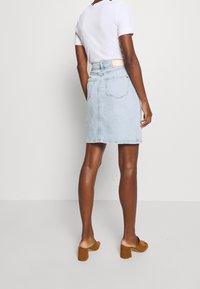 Hame sinimarle sa denim, muotoiltu tiivisti, keskipitkä leikkaus ja kaksi takataskua. Yhdistetty valkoiseen lyhythihaiseen paitaan ja ruskeisiin paksupohjaisiin sandaaleihin.