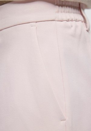 Primo piano di pantaloni rosa chiaro che mostrano una coulisse elastica in vita e la cucitura della tasca laterale con una texture di tessuto liscia.