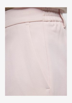 Gros plan sur un pantalon rose clair montrant une ceinture élastique et une couture de poche latérale avec une texture de tissu lisse.