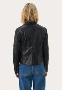 Veste en cuir noir au design ajusté, dotée d'un col haut, de coutures détaillées et de poignets zippés, associée à un jean taille haute bleu.
