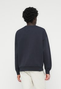 Sweatshirt azul-marinho com decote redondo, punhos e bainha canelados. Feito de um tecido suave, apresenta costuras de ombro caídas e um design simples.