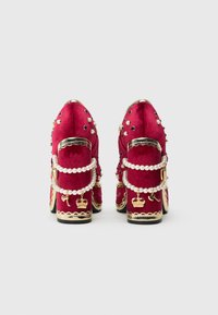 Κόκκινα βελούδινα τακούνια με χρυσές λεπτομέρειες, λουράκια από πέρλες και διακοσμητικά καρφιά. Διαθέτουν διακοσμητική κορώνα και γούρι στα πλάγια.