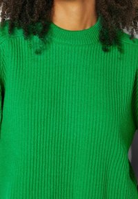 Zelený žebrovaný svetr s kulatým výstřihem, měkkou texturou a přiléhavým střihem, který zdůrazňuje vertikální linie po celé látce.