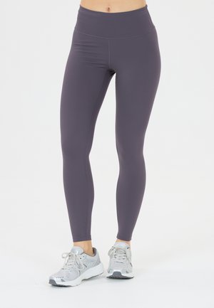 Hoge taille leggings in donker lavendel, gemaakt van rekbare stof. Heeft platte naden en is gecombineerd met lichtgrijze sportschoenen.